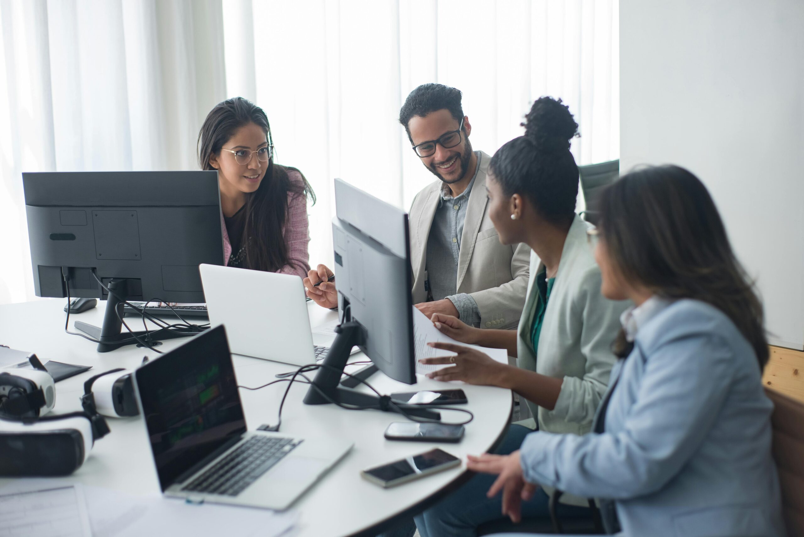 A diverse team engages in discussion around computers in a modern office setting.